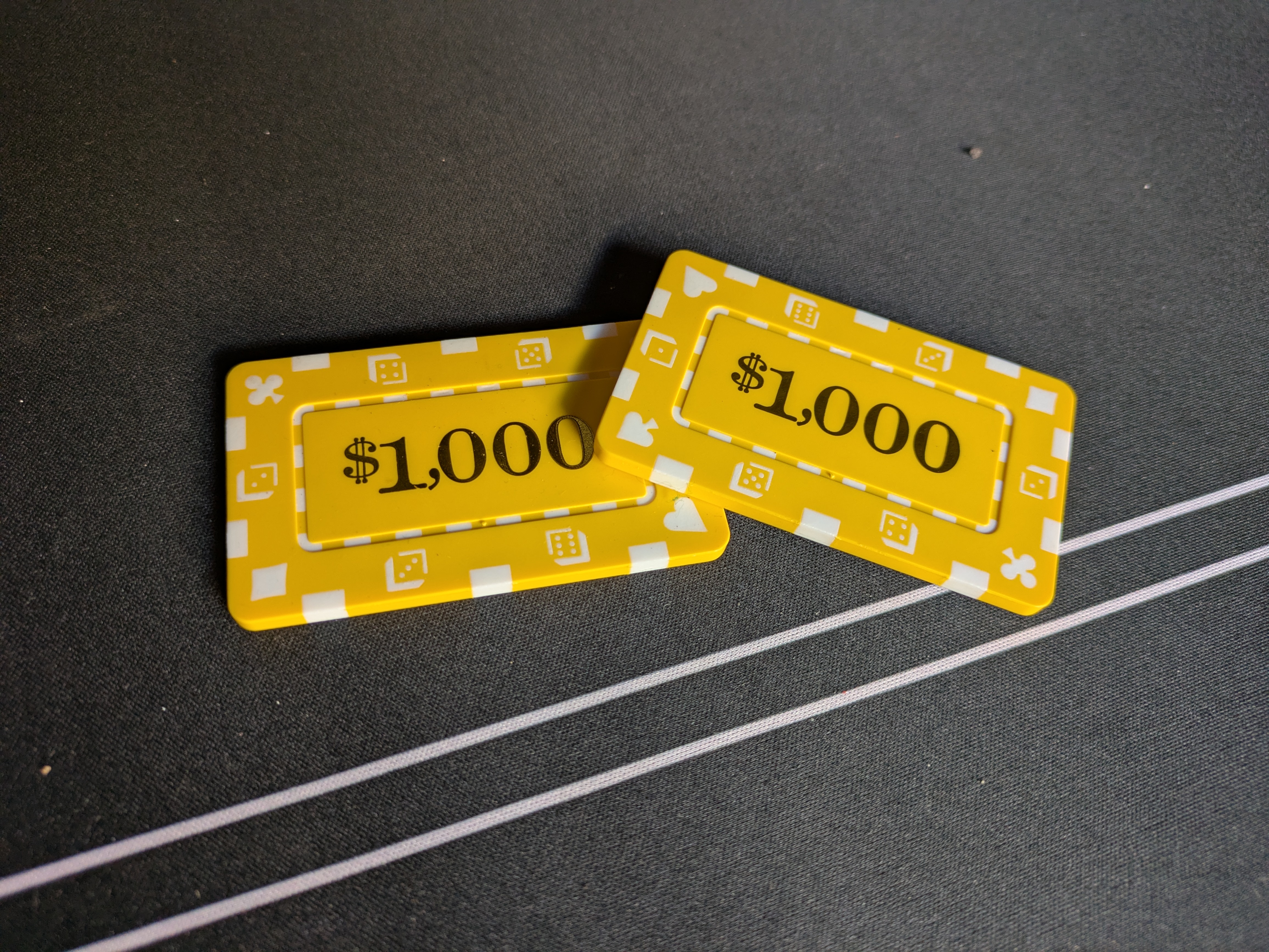 Two yellow $1,000 casino plaques on a dark gaming mat.